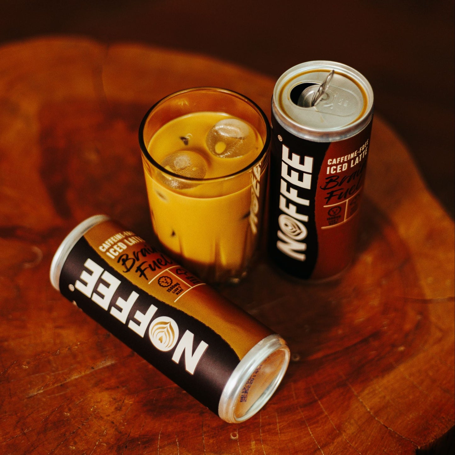 Two cans of 'Noffee' and a glass of iced Noffee on a wooden surface.